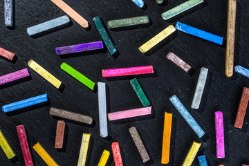 Colorful wallpaper pattern with colored chalks on black background of chalkboard, back to school concept, flat lay