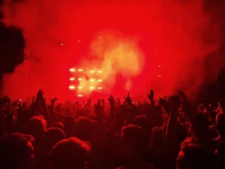 A crowd with their hands up in the air under the scene in red smoke