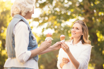 Amused young woman tasting ice cream with aged mother outdoors