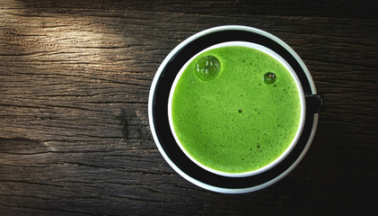 Green tea in black cup on wooden desk with sunlight , copy space