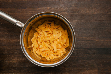 Colorful cooked fettuccine in pan closeup. Yellow tagliatelle top view culinary background with free space
