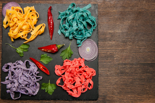 Colorful tagliatelle with spices on black plate on table. Food concept top view, copy space wooden background