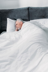 portrait of pensive senior man lying in bed at home