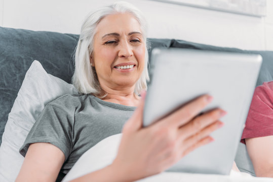 portrait of smiling woman using tablet while lying in bed at home