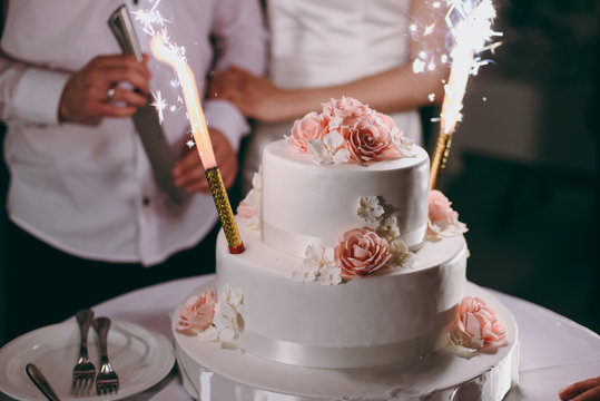 Beautiful white and colored wedding cake. A bride and a groom is cutting their wedding cake