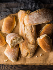 Freshly baked bread loaves on burlap dark wooden background. Texture closeup italian bakery products