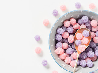 Round purple and pink bonbon candies sweets in gray bowl on white canvas background. Minimal still life