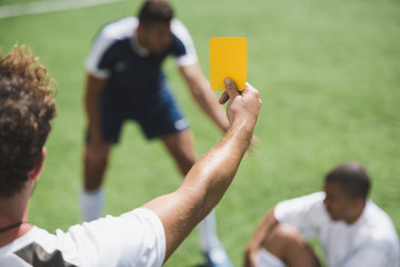 back view of soccer referee showing yellow card to players during game