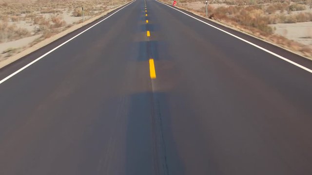 AERIAL TILTING UP: Flying above an empty road past grey sandstone desert in Utah flatlands, USA. Traveling on road trough rocky desert landscape, past the sandy dunes on sunny day. Summer road trip