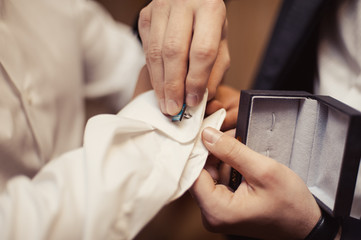 Fototapeta na wymiar The groom fastens the cufflink on the shirt sleeve close-up