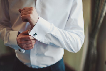 The groom fastens the cufflink on the shirt sleeve close-up