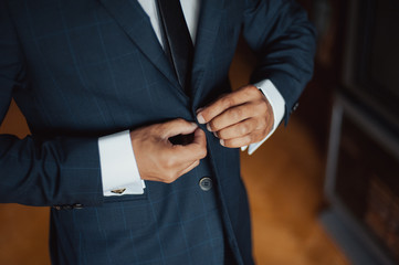 Elegant groom in wedding jacket wearing white shirt and turquoise tie. Groom's hands on blue suit.