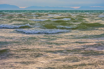 Sun rays reflecting on the surface of green sea waves with mountains in the background
