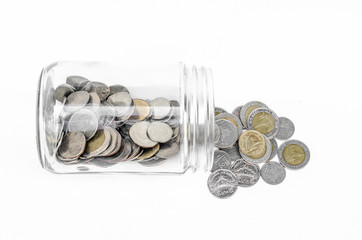 many coins spilling out of a glass jar and isolated on a white background