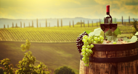 Naklejki  Butelka czerwonego wina i kieliszek do wina na drewnianej beczce. Piękne tło Toskanii