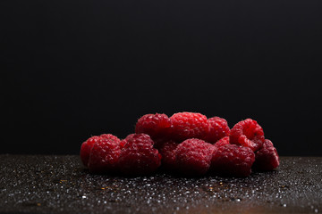 A pile of raspberries on black background with drops of water