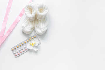 Pregnancy planning. Contraceptive pills and booties on white background top view copyspace