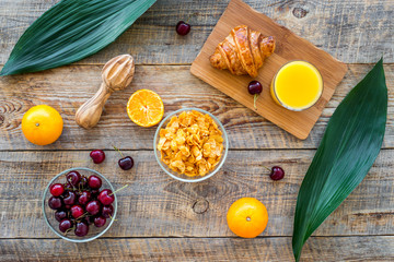 Preparing healthy summer breakfast. Muesli, oranges, cherry, juice on wooden table background top view