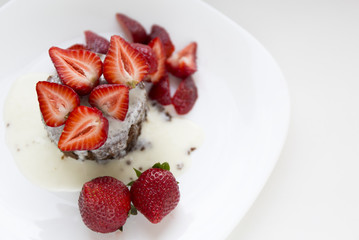 Delicious homemade chocolate cake with fresh red strawberries and cream sauce on white plate.