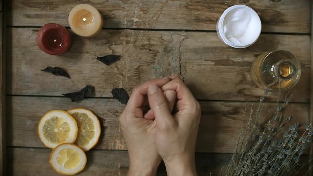 Woman applying moisturizing soft cream and massaging her hands over wooden table background.  