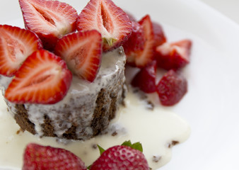 Delicious homemade chocolate cake with fresh red strawberries and cream sauce on white plate.