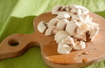 The process of cutting champignon mushrooms on a wooden cutting board
