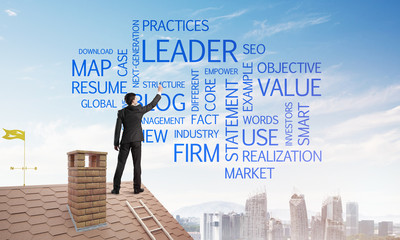 Young businessman standing on house roof and writing leadership skill concept. Mixed media