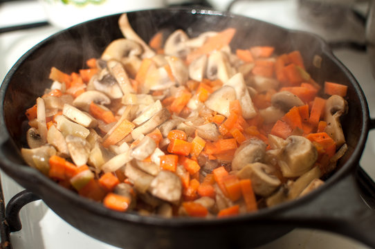 Delicious fried mushrooms champignons, carrot and onion in pan on gas stove