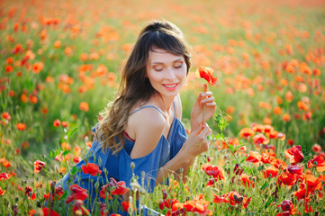 Naklejka na ściany i meble Beauty woman in a blue dress smiles in a poppy field at sunset, cleanliness and innocence, unity with nature