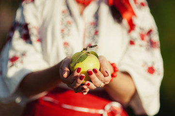 A girl in an embroidery is holding an apple in her hands