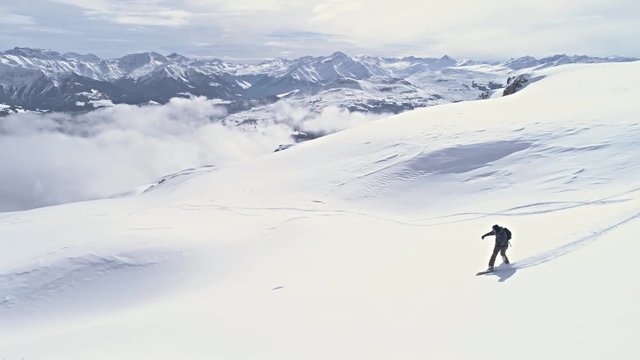 Aerial footage of a snowboarder going down the backcountry in a winter resort in Switzerland. Drone footage in slowmotion in 4k quality.