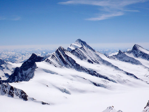 two mountain climbers on a narrow and exposed snowy summit ridge with a spectacular view of the Swiss Alps