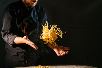 Chef's hands toss and shake the ribbon-like Italian pasta over the wooden kitchen table before...