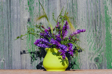 A bouquet of purple wild flowers in a yellow ceramic vase on old wooden background wall, vintage
