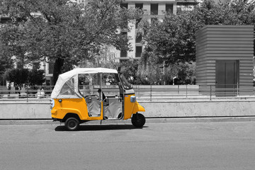 Black and white picture of tuk tuk small passenger three weel mini car isolated on summer empty street road background. Bright yellow rickshaw helps tourists to travel around the city fast