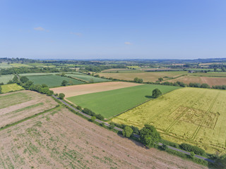 Aerial view of green wheat and ploughed farm fields, with a crossing country road, in an English countryside, on a sunny summer day .