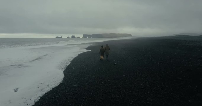 Aerial view of the hipster couple walking on the shore of the sea, in black volcanic beach in Iceland together.