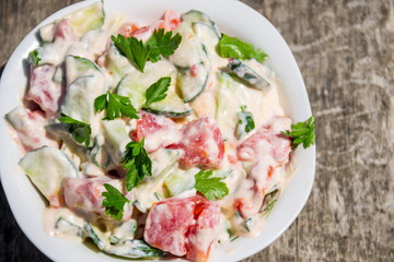 Fresh salad with tomato, cucumber, onion, parsley and mayonnaise on rustic wooden table