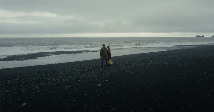 Aerial view of young couple standing on black volcanic beach near the troll toes rocks and enjoying on wave in Iceland.