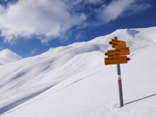 hiking trail markers in the Swiss Alps in winter with snow and mountain peaks with fresh ski tracks from back country skiers
