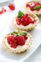 Dessert tartlets with berries on white wooden background