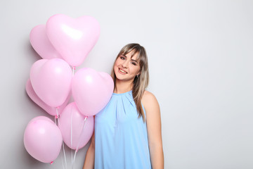Portrait of young woman with pink heart balloons on grey background