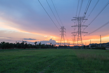 Group silhouette transmission towers (steel lattice/power tower, electricity pylon) next to apartment complex at sunset in US. Texture high voltage pillar, overhead power line, industrial background.