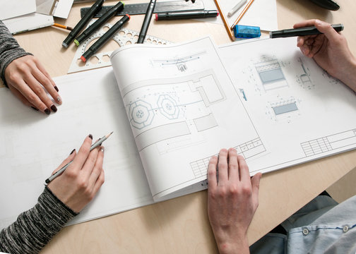 Designers hands drawing scheme of piece of furniture on creative desk top view. Unrecognizable man and woman working together in architecture workplace