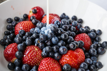 Strawberries, blueberries and milk in a white bowl