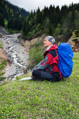 Smiling man traveler is relaxing on the shore of a mountain river