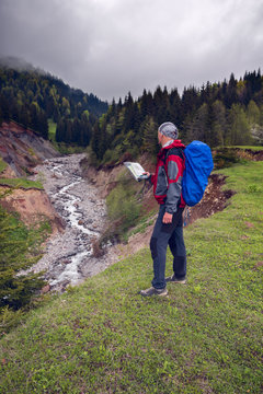 Traveler with map on shore of a mountain river
