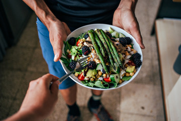 POV of man hands holding big deep plate full of healthy paleo vegetarian salad made from fresh...