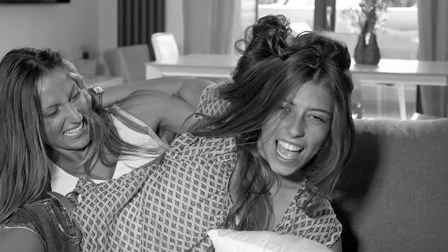 Two girlfriends fighting hard on sofa pulling hair 1 black and white