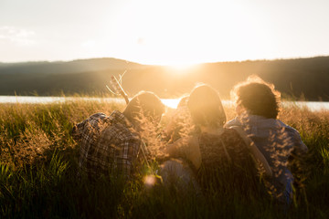 Friends sitting together at lake enjoying sunset